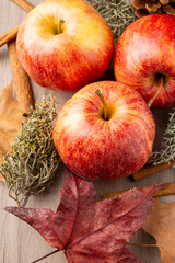 Aerial view of three red royal gala apples with cinnamon sticks and autumn leaves on wooden table in vertical