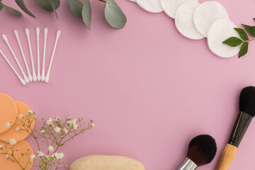 Makeup brushes, cotton buds, cotton pads and plants on pink background