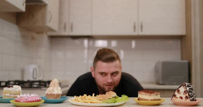 The hungry man is quickly eating the french fries and burger and hidding with the plate behind the kitchen furniture.