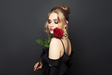 Young perfect woman with blonde hair and makeup holding red rose flower on black background
