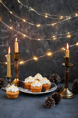 Muffins with butter cream in a vintage plate on a wooden high stand. New Year's festive desserts on the table with a garland and candles.