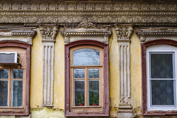 An old house with a stucco ornament, a fragment of the facade with windows. The picture was taken in Russia, in Orenburg