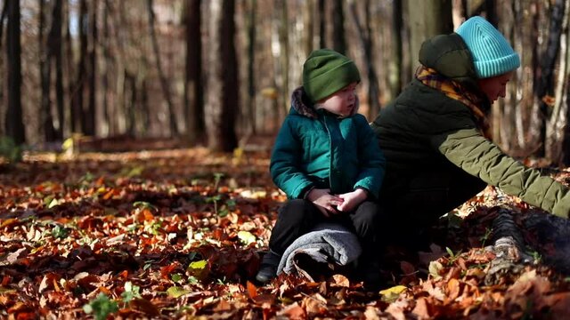 Little caucasian boy with young mother sitting near the fire enjoying autumn forest nature. Sunny background. Family healthcare. Green tourism. Traveling lifestyle. Weekend outdoor. Smiling male child