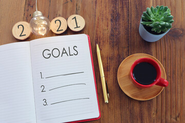 Business concept of top view 2021 goals list with notebook, cup of coffee over wooden desk