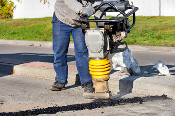 Fototapeta premium The road worker holds a bouncing vibratory rammer when repairing the roadway.