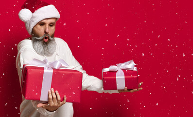 man in a Santa hat with a surprised and embarrassed expression looks at the gifts he is holding in his hands. A man does not know which gift to choose. snowing