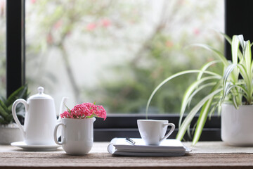 Panama Rose and white teapot and cup with notebook and green plant on wooden table
