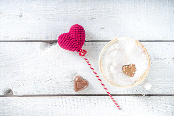 Girl hands hold hot chocolate or coffee latte cup with marshmallow hearts  above wooden background copy space