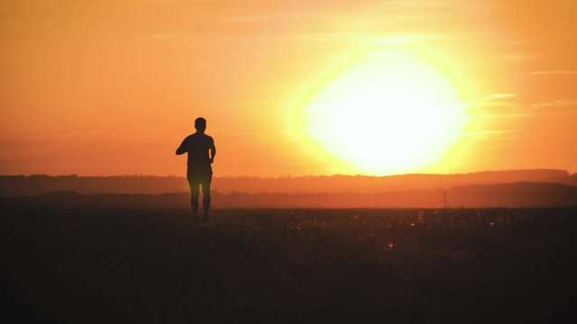 Running man silhouette in sunset time. Outdoor cross-country running. Athletic young man is running in the nature during golden sunset. Healthy lifestyle.