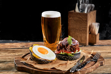 Good Burger, with beef, onions, sweet onions, cheese, lettuce, tomato on craft paper with glass of beer on the background