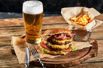 A large mouth-watering burger with grilled beef patty and fresh vegetables. Tasty american cheeseburger on a wooden board. Classic homemade burger in craft paper.