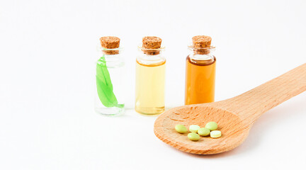 Several bottles of oils and green leaves and a number of vitamins in a wooden spoon.