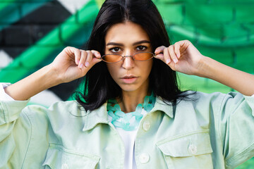 brunette girl with a serious face looks at the camera and holds fashion glasses with her hands. High quality photo