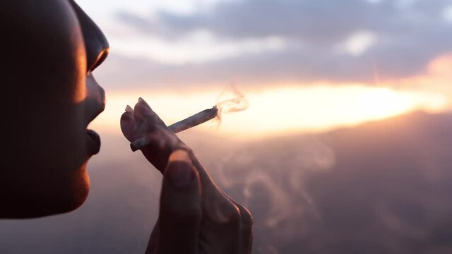 Slow motion of woman smoking weed cannabis joint with sunlight at sunset time.