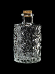 Empty glass bottle with facets, closed with a cork, isolated on a black background.