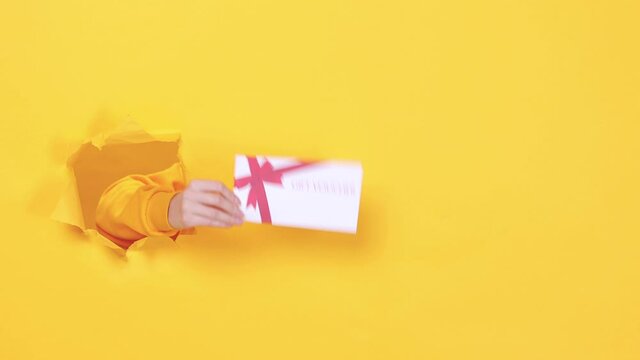 Close up cropped woman hand hold gift certificate card coupon voucher on birthday holiday party or store isolated through torn yellow background studio. Copy space text place. Advertising area mock up