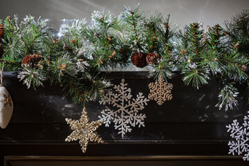Pine branch with cones, snow, white and gold snowflakes on the black surface of the fireplace. Daylight. Happy Merry Christmas.