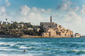 Old Jaffa city, old port and coastal line of Tel Aviv under sunset and lots of tourists are swimming and surfing at the Mediterranean sea.