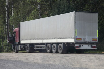 European semi truck with gray tented van trailer parked on roadside Parking at summer day on green forest background, driver work time vacation, Cargo logistics, goods delivery on road transportation