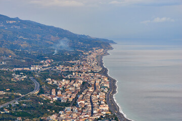 Fototapeta premium the eastern coast of Sicily seen from above with its towns, roads, railways, buildings and highways on a partially covered autumn day