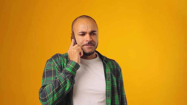 Worried anxious man talking on mobile phone against yellow background