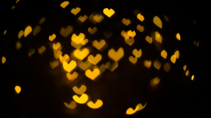 Bokeh on a black background for use in the photo editor. Beautiful bright curly bokeh. Magic background for new year and Christmas. Banner with yellow unfocused lights garlands in the shape of heart.