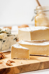 Pieces of camembert cheese with white mold on a wooden cutting board close-up.