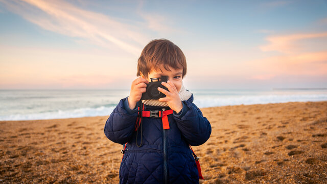 Little boy pretending to take a picture with compact camera on beach at sunset, winter season.