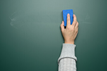 woman's hand wipes a green chalk board with a blue sponge © nndanko