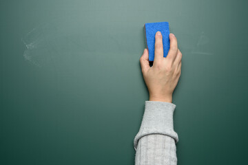 woman's hand wipes a green chalk board with a blue sponge