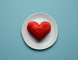 Fototapeta na wymiar red heart lies in a white ceramic plate on a blue background