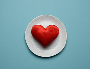 red heart lies in a white ceramic plate on a blue background