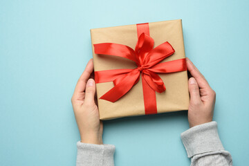 two female hands in a sweater hold a square gift box with a red bow