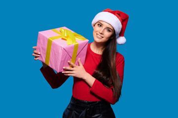Fototapeta na wymiar Woman in Santa's hat holds Christmas gift box over blue isolated background. New year and Christmas celebration concept