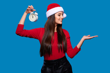 Fototapeta na wymiar New year mock-up, Christmas template. Smiling woman in Santa Claus hat with clocks and holds on palm copy space for advertising