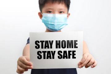 Portrait of a 9-year-old Asian boy wearing a protective mask and holding a paper card with text Stay Home Stay Safe.