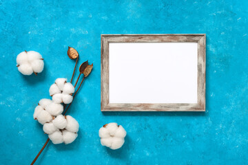 Blank portrait frame mock up and cotton flowers on a blue grunge background. Template for your design. Top view, flat lay, copy space.
