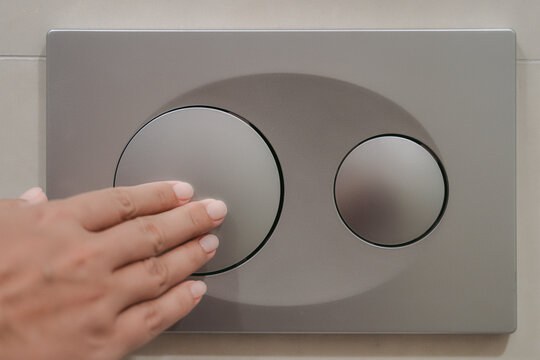 Woman pushing one button of two on wall of bathroom to flush toilet.