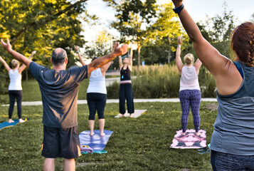 A group of adults attending a yoga class outside in park