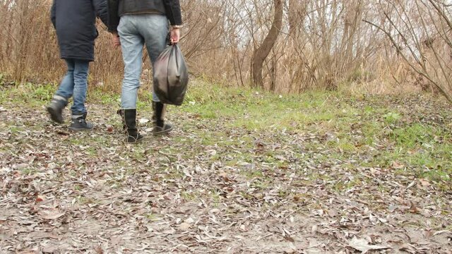 A girl and a child are walking through the forest. The girl carries a bag of rubbish. Close-up. Fall. Ecology
