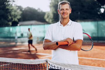 Portrait of positive male tennis player with racket standing at clay court