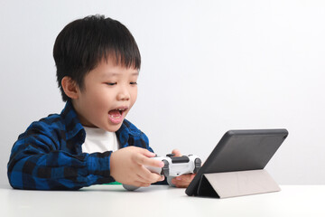 Portrait of a 9-year-old Asian Boy playing video game with a game controller at his desk at home.
