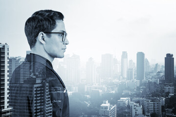 Young handsome businessman in suit and glasses dreaming about new career opportunities after MBA graduation. Bangkok on background. Double exposure.