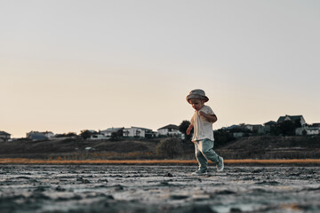 Two-year-old child in a hat walks along a country road, summer. Knowledge of the world.