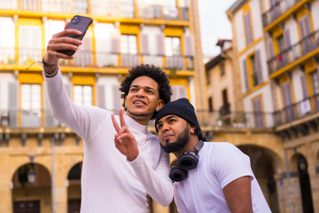 Lifestyle, two black Latino friends taking a nice selfie on the street. Boy with afro hair and boy with hat and earphones