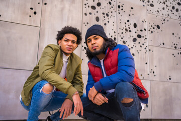 Urban style, portrait of two Latino black friends having fun in the street. Afro hair boy, brunette boy with long hair with hat