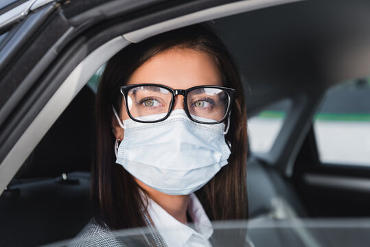  Businesswoman In Eyeglasses And Medical Mask Looking Out From Open Window While Riding In Car