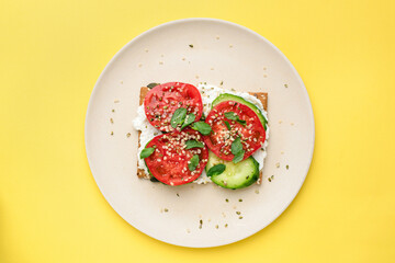 Rye crispbread or cracker with vegan cream cheese, tomato, cucumber and hemp seeds isolated on yellow background. Top view. Healthy appetizer or snack