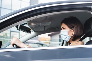 side of woman in medical mask looking ahead while driving car