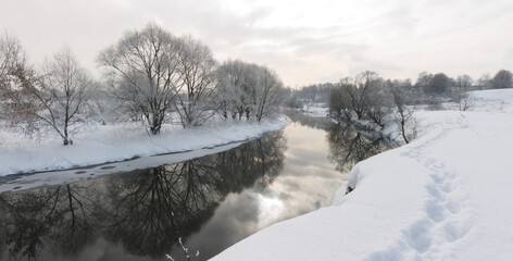 Photo the snow-covered river did not freeze in winter.The river flows in winter. Snow on the branches of trees. Reflection of snow in the river. Huge snowdrifts lie on the Bank of the stream.